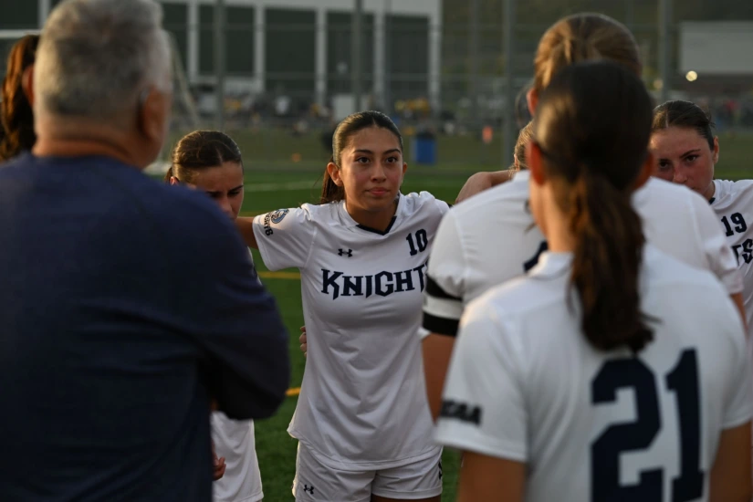 female soccer players and coaches huddle on the field