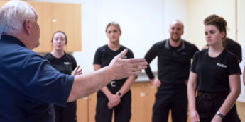 Students wearing black stand in a group while receiving direction from professor