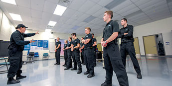 Students standing at attention while professor gestures and speaks