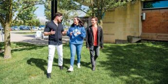 Three students walking in the grass on campus.