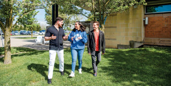Three students walking in the grass on campus.