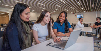 Three female students are sitting together and studying at a laptop.