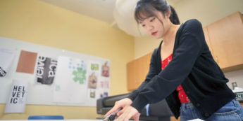 Student using cutting tool while working on art project in design classroom