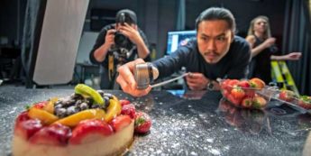 Student takes a photograph of an appealing fruit cheesecake while another student holds up a flash