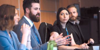Students at conference in professional attire applauding from speaker's table