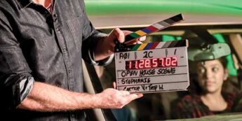 Man with clapper with women in car filming on a green screen.