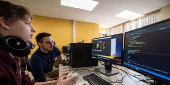 Two male students in the game design lab with multiple monitors.