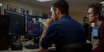 Two male students in the game development lab with multiple monitors.
