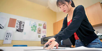 Student using cutting tool while working on art project in design classroom