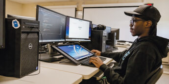 male student working on multiple computer screens using a coding software program