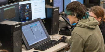 two students sitting in front of computers working on game design