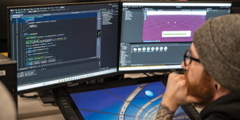 male student looking at computers working on game development