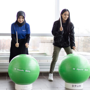 Two students playing large green drums in the shape of balls