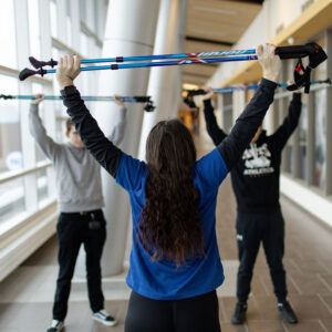 Student stretching above her head with hiking poles