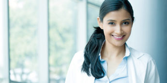 Female Indian student wearing white lab coat smiling at camera