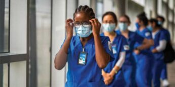 Students dressed in blue scrubs and face masks walk down a hallway