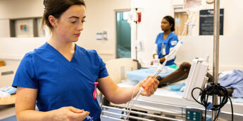Student nurse in training adjusts an IV drip in nursing lab