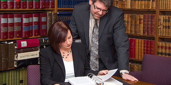Lawyer looks over page while  law clerk student reads through binder of papers