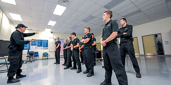 Students standing at attention while professor gestures and speaks