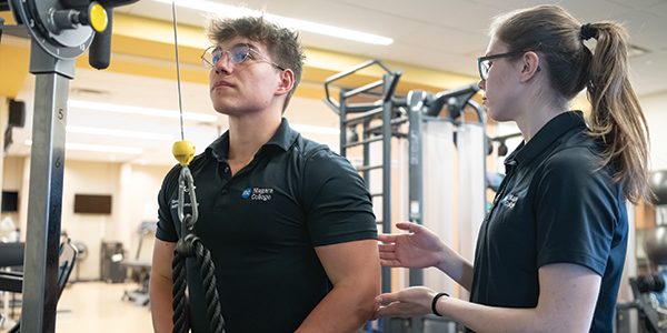 Female student teaching a client how to use an exercise machine in the gym