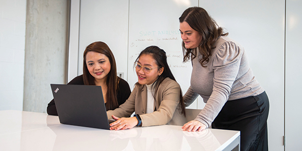 three female students are focused on a laptop, engaged in conversation while looking at the screen