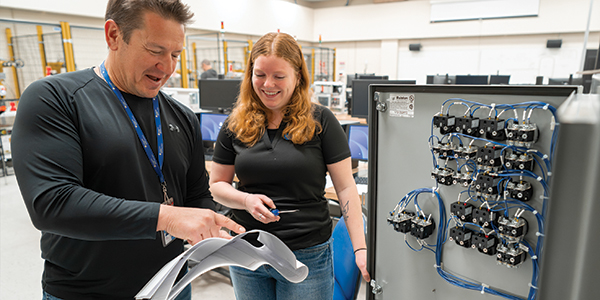 instructor and student looking at instructions beside electronic equipment in classroom