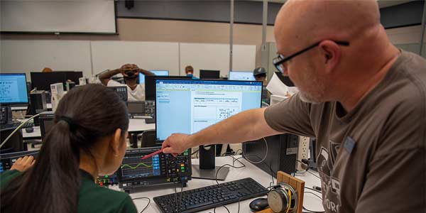 Teacher explaining something to a student sitting at a computer.