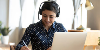 A young woman works on computer with a headset and microphone