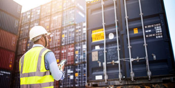 Man wearing hard had and safety vest next to shipping containers
