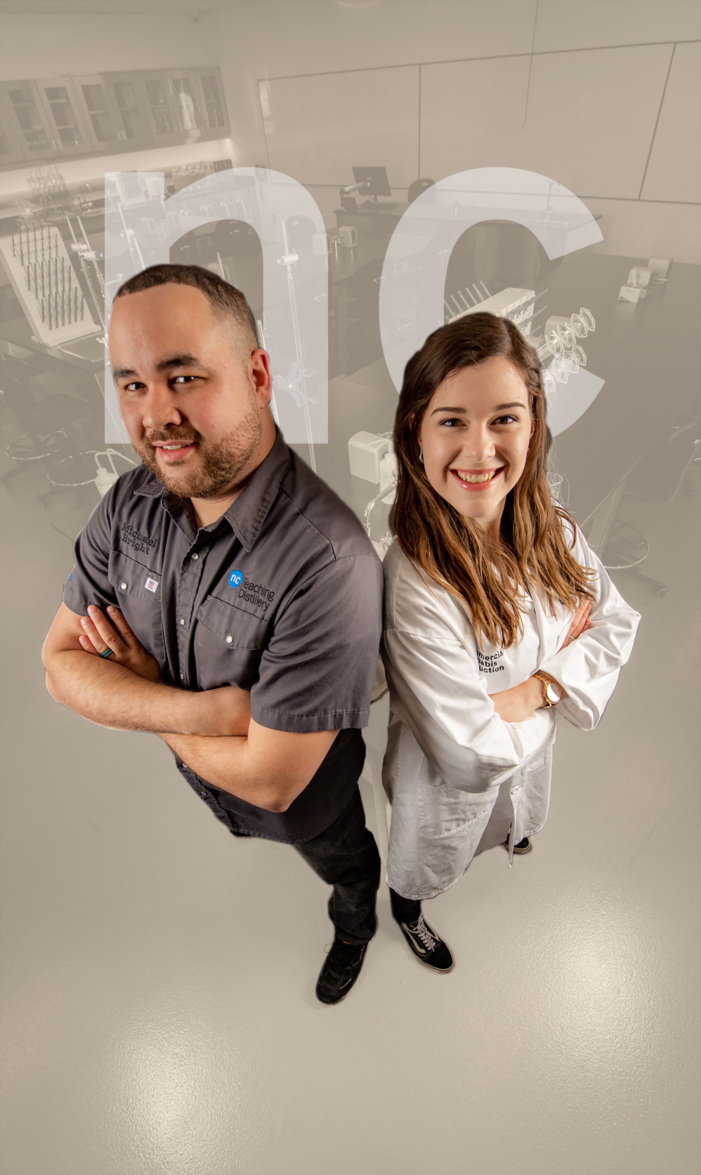 A woman wearing a NC lab coat and a man wearing a NC shirt stand back to back with arms crossed