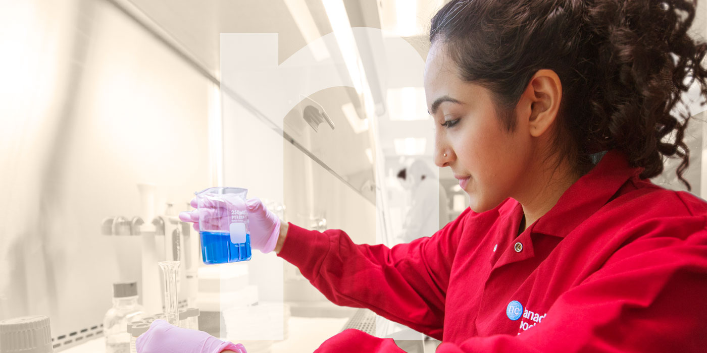 Woman wearing labcoat pouring a vial into another vial