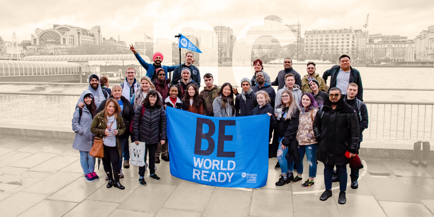Group of students outside overseas holding a Be World Ready NC flag