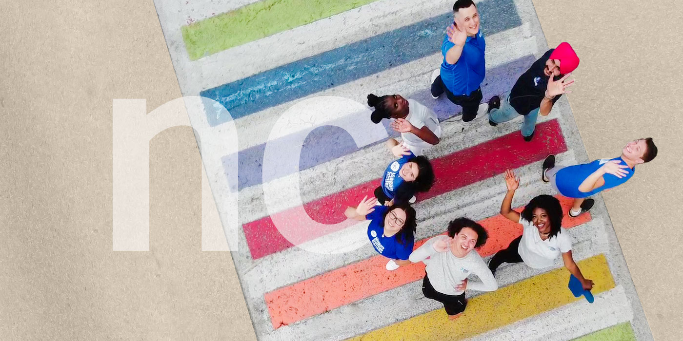 Ground of students in a circle looking up while standing on a rainbow crosswalk