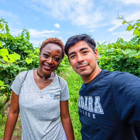 Two diverse students wearing NC shirts take a selfie in a vineyard