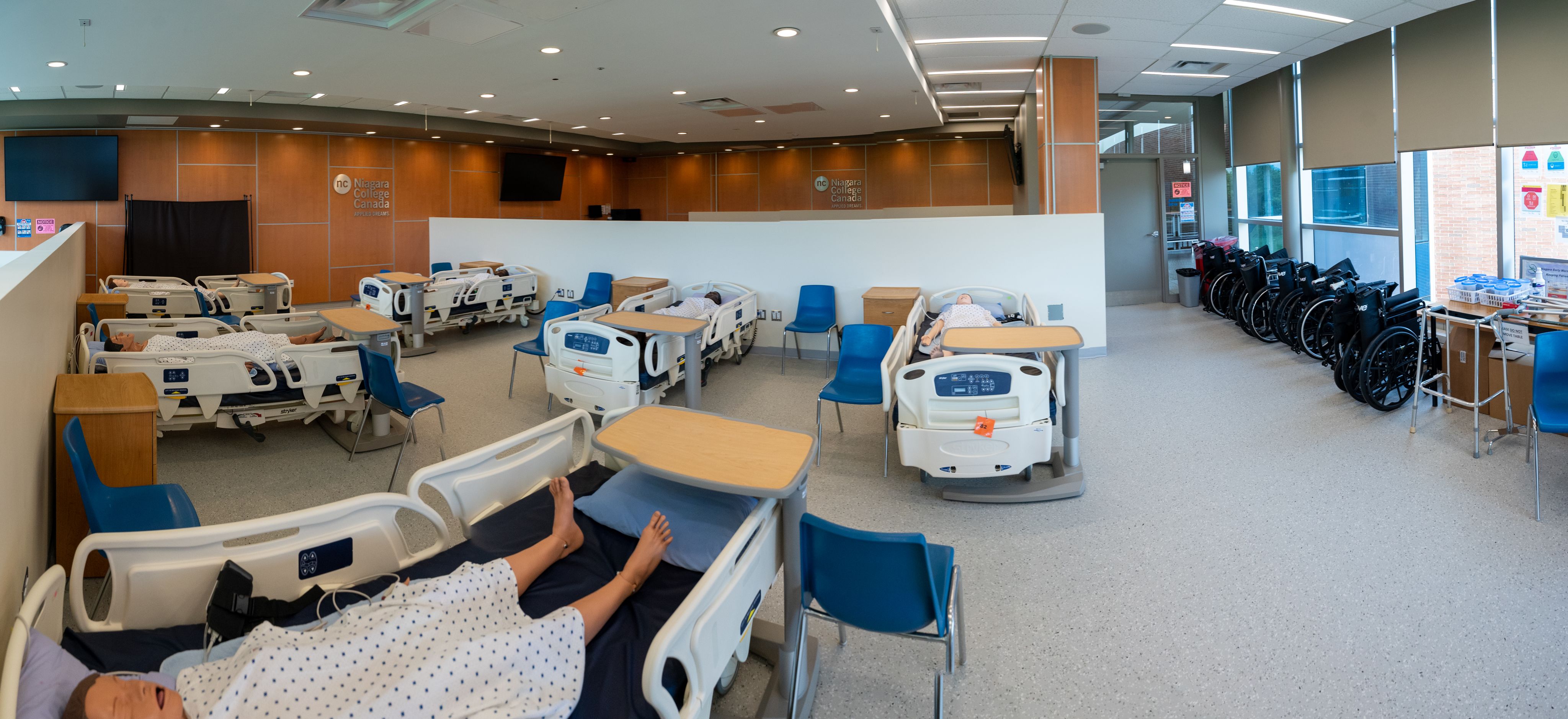 A clinical lab classroom with hospital beds and wheelchairs.