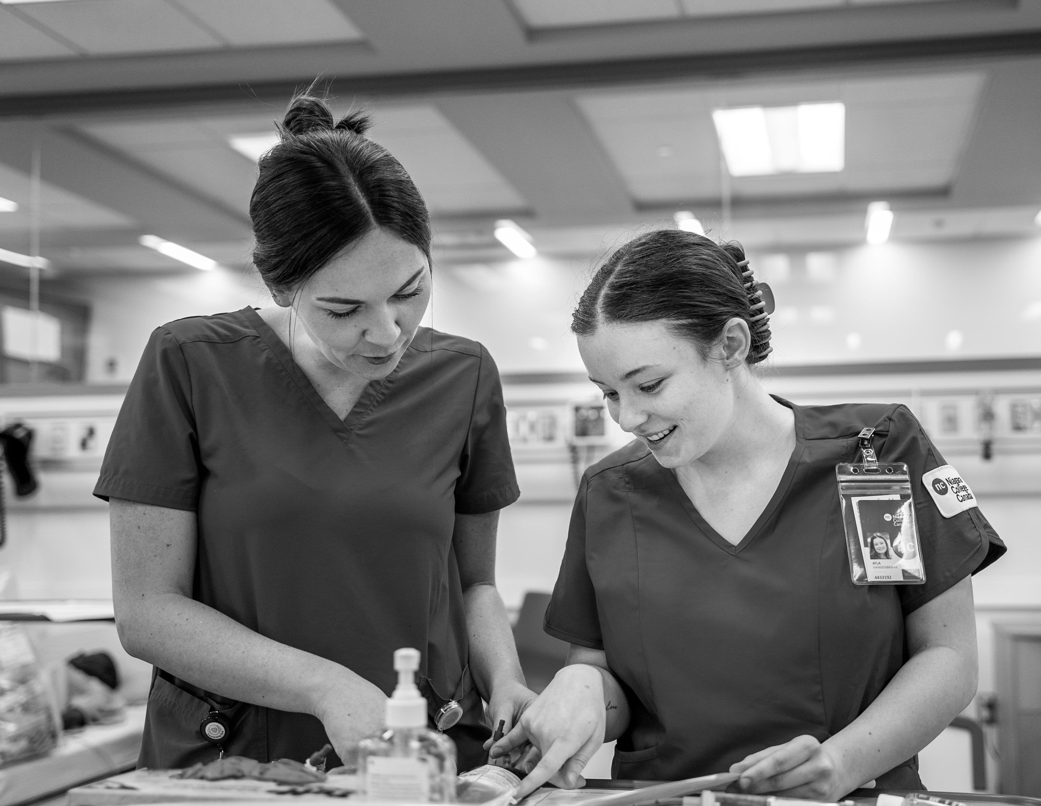 Two female students wearing scrubs reviewing patient information.