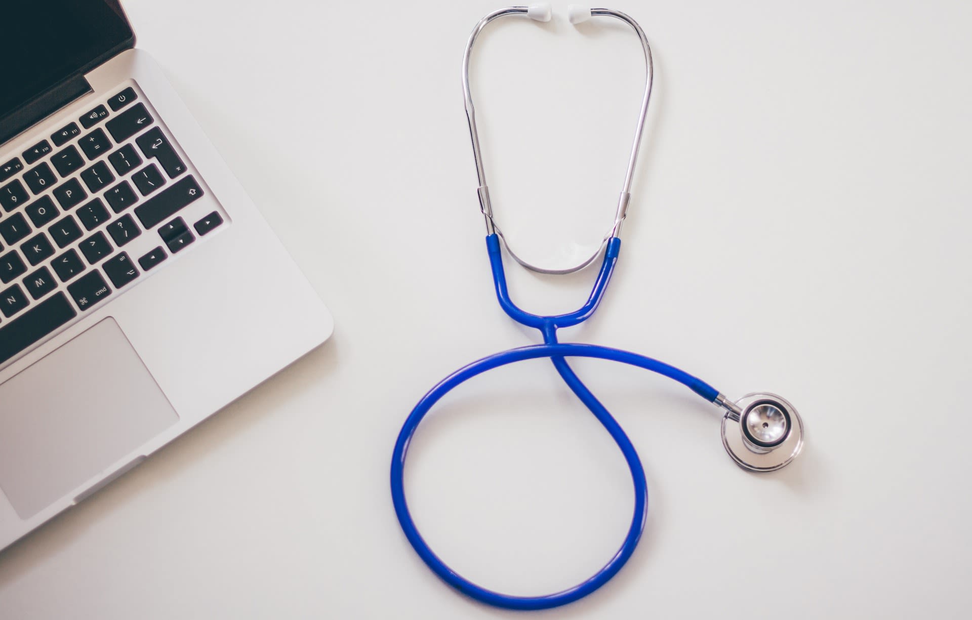 A blue stethoscope rests beside a laptop.
