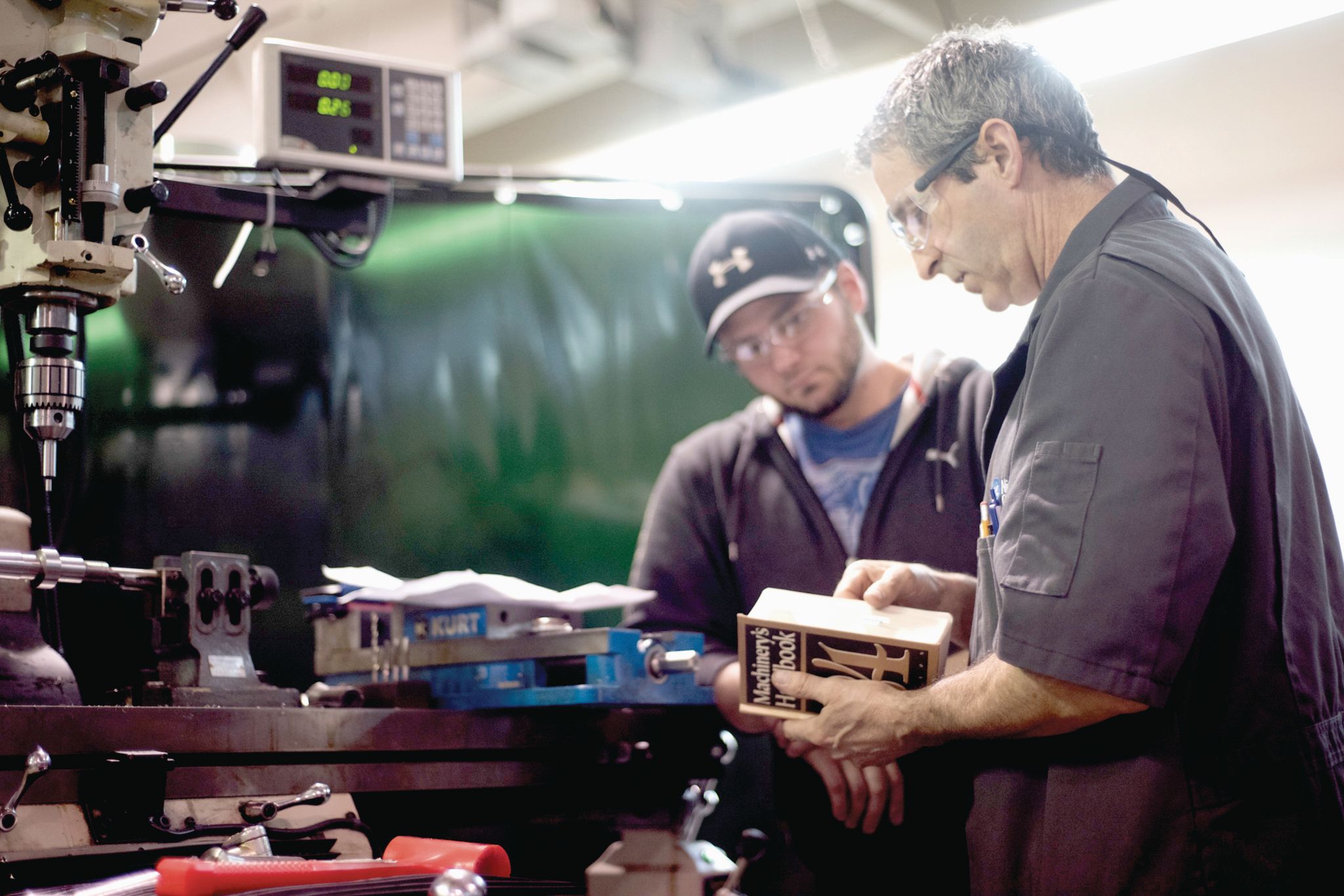 Two male machinists stand together reviewing an inspection booklet.