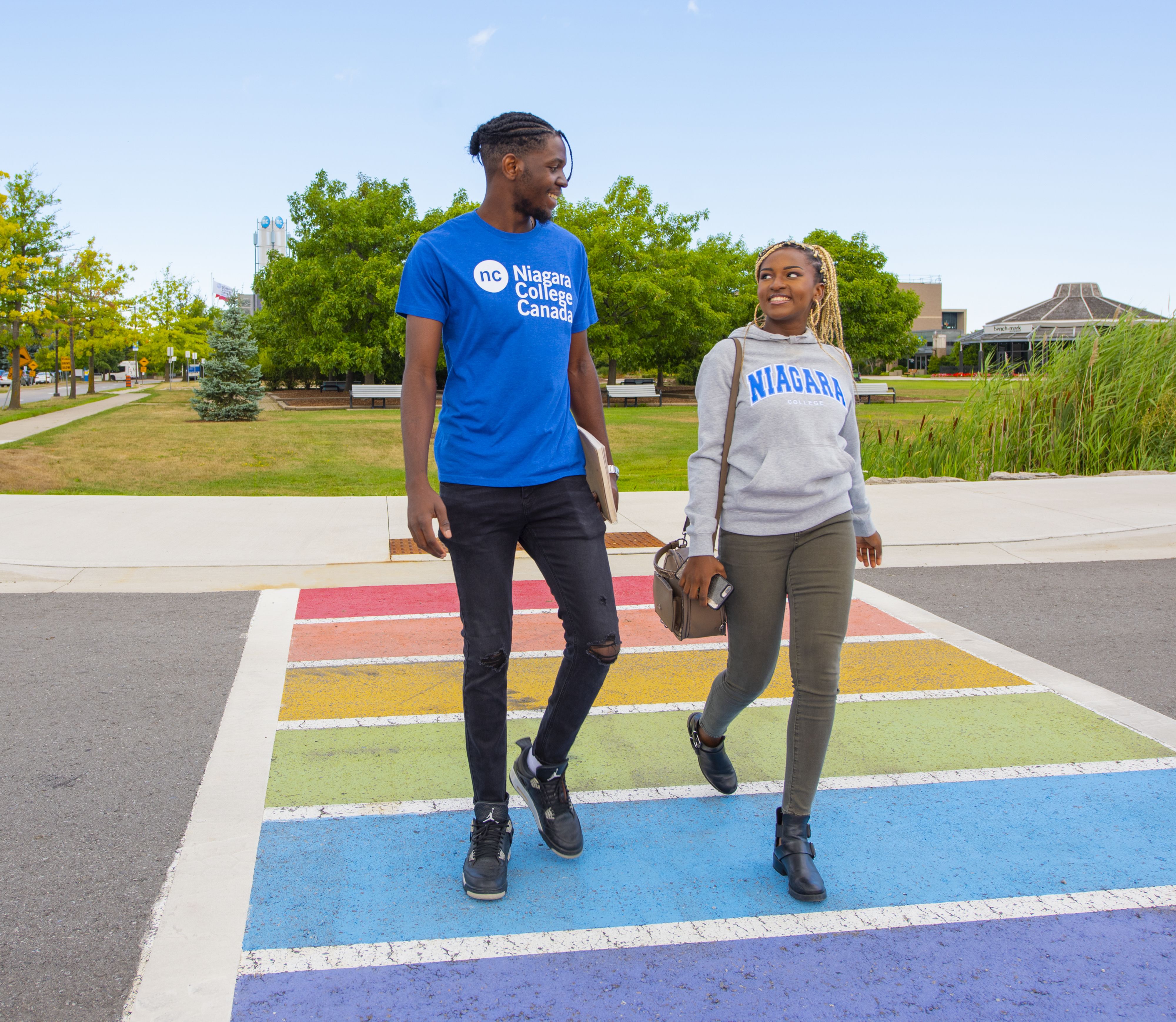 Male and female student walking across rainbow coloured crosswalk.