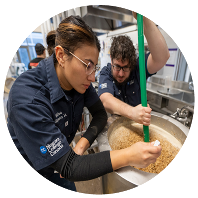 Female and male student stirring ingredients for beer production.