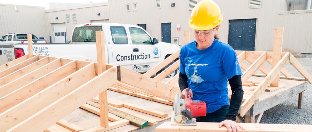 Female student wearing a hard hat and holding a saw.