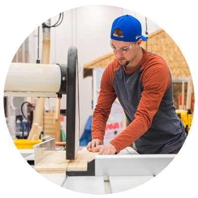 Male carpentry student using table saw to saw a piece of wood.