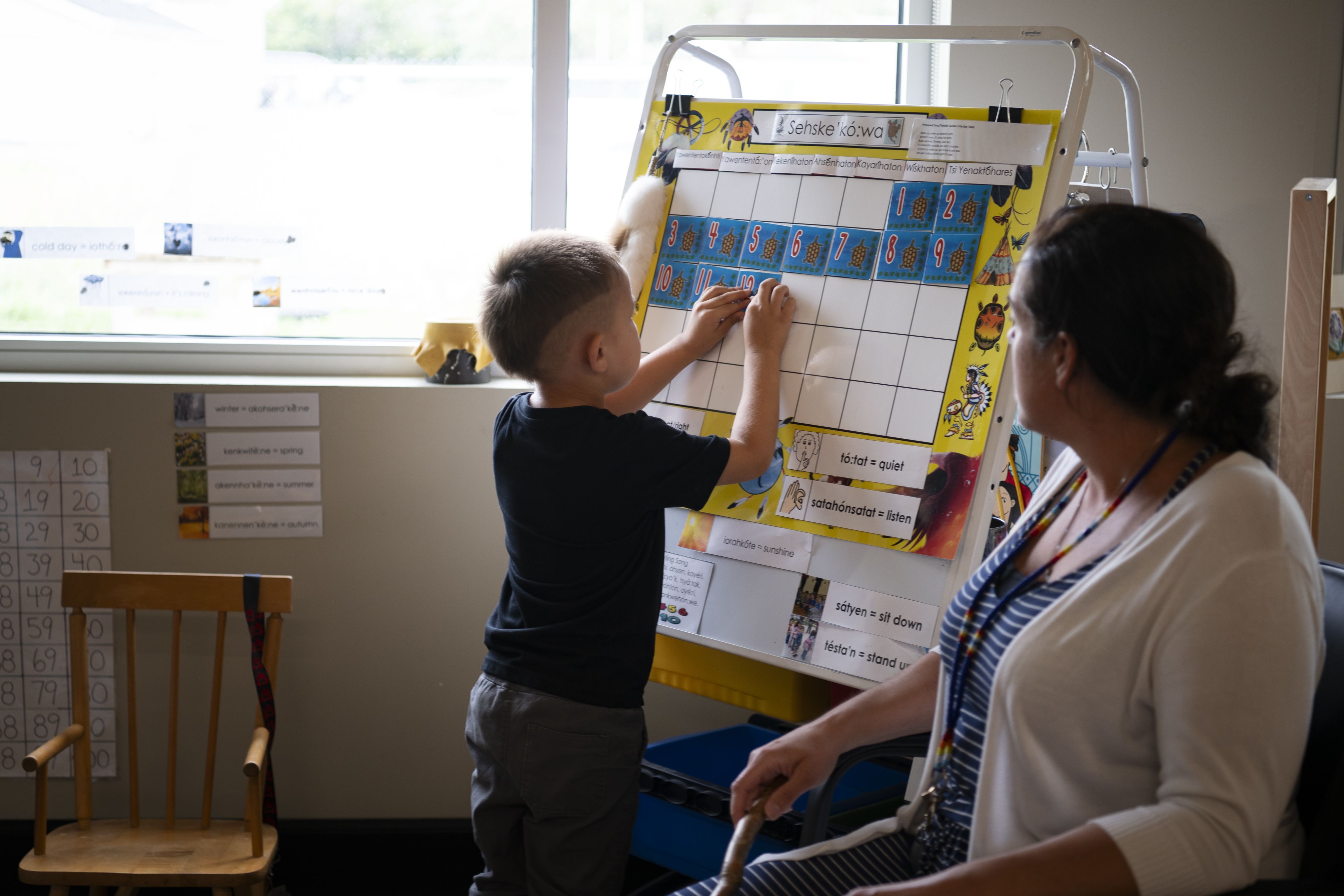 Mother watching a young boy add numbers to an activity board.
