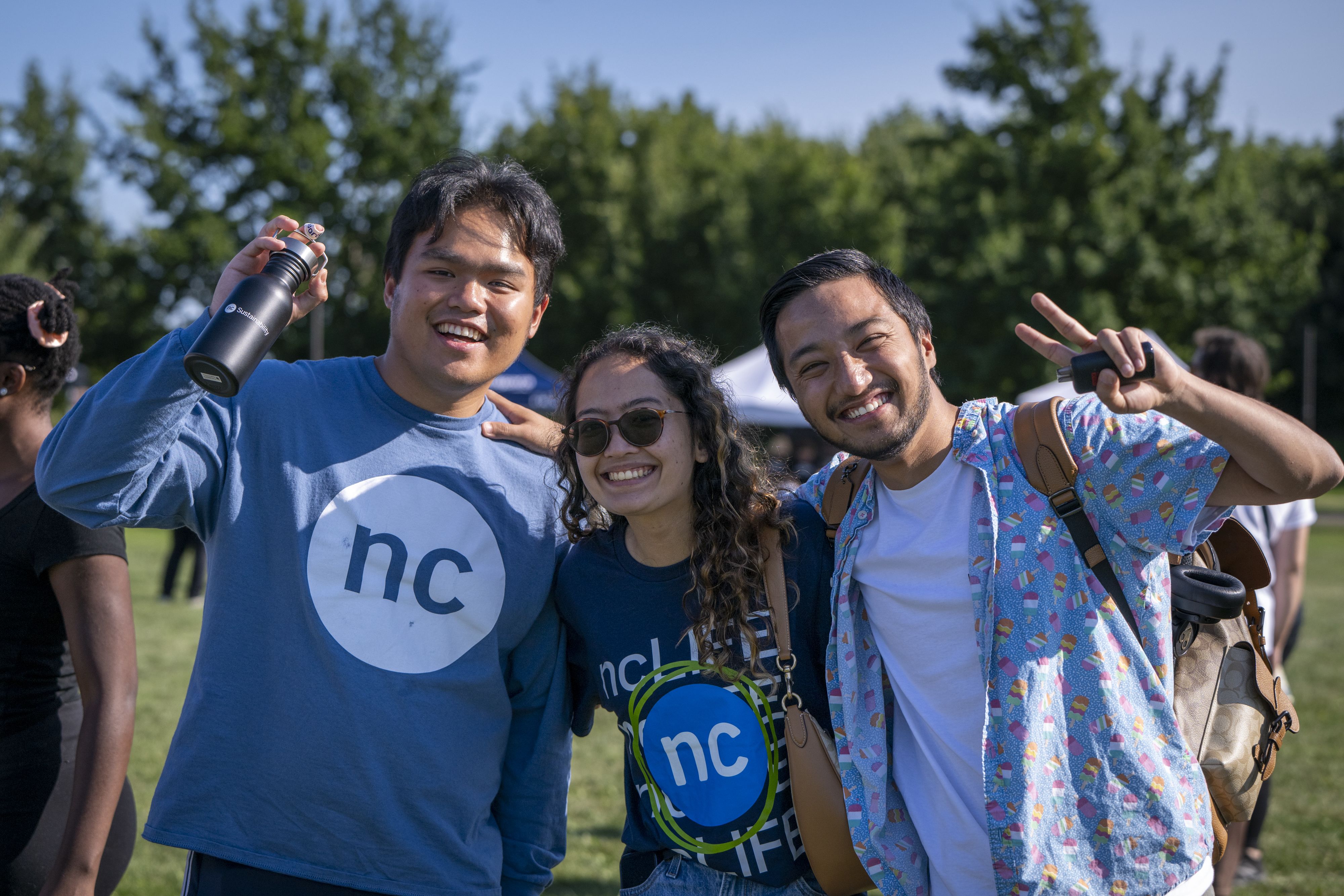 Three students stand together outside smiling and wearing Niagara College shirts.