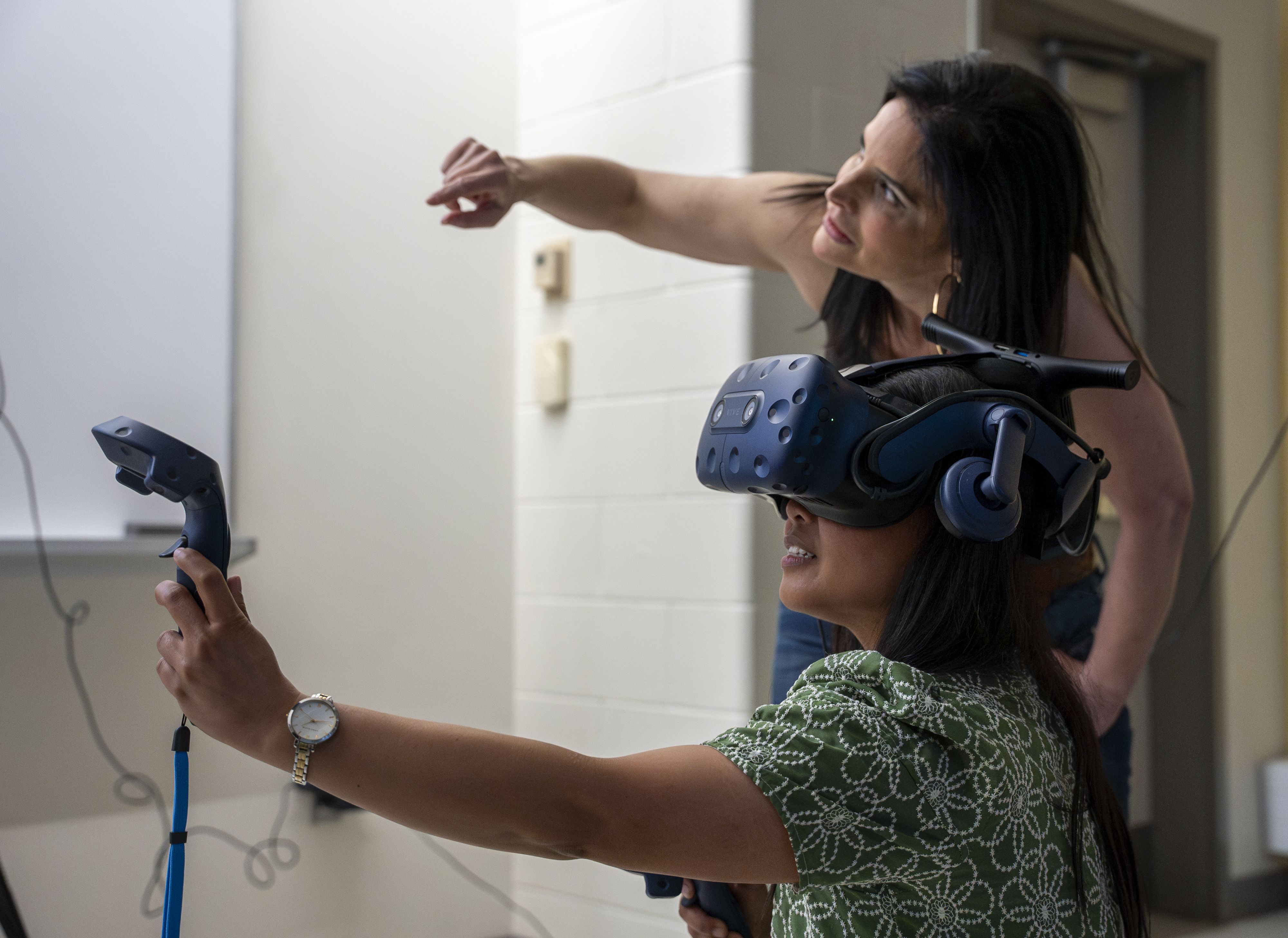 A female student wears a virtual reality headset engaged in an immersive learning experience while a female professor stands nearby.