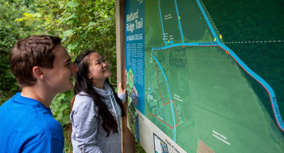 Two students consult the Wetland Ridge Trail map sign board at the NOTL campus