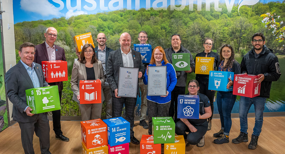Group of NC staff poses with 2 large certificates for the UN Sustainable Development Goals signing pledge