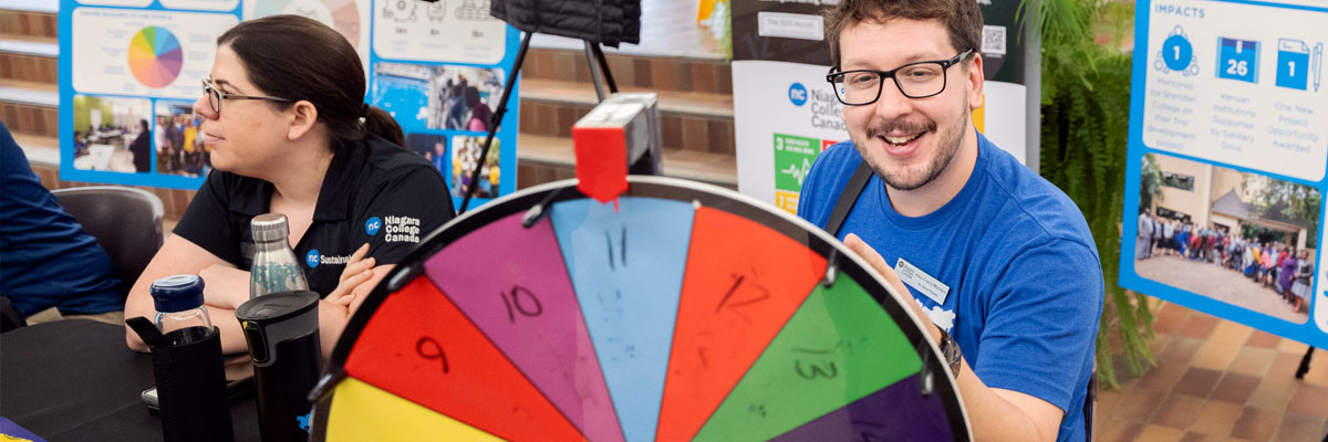 A student volunteer mans a Sustainability information booth featuring colourful posters and displays