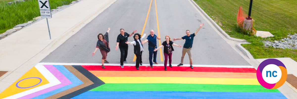NC executive team poses on the rainbow crosswalk outside of the NOTL campus - featuring overlay of the NC Equity Diversity and Inclusion logo