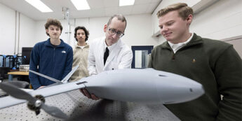 A group of students with faculty examine a model drone in a lab setup.